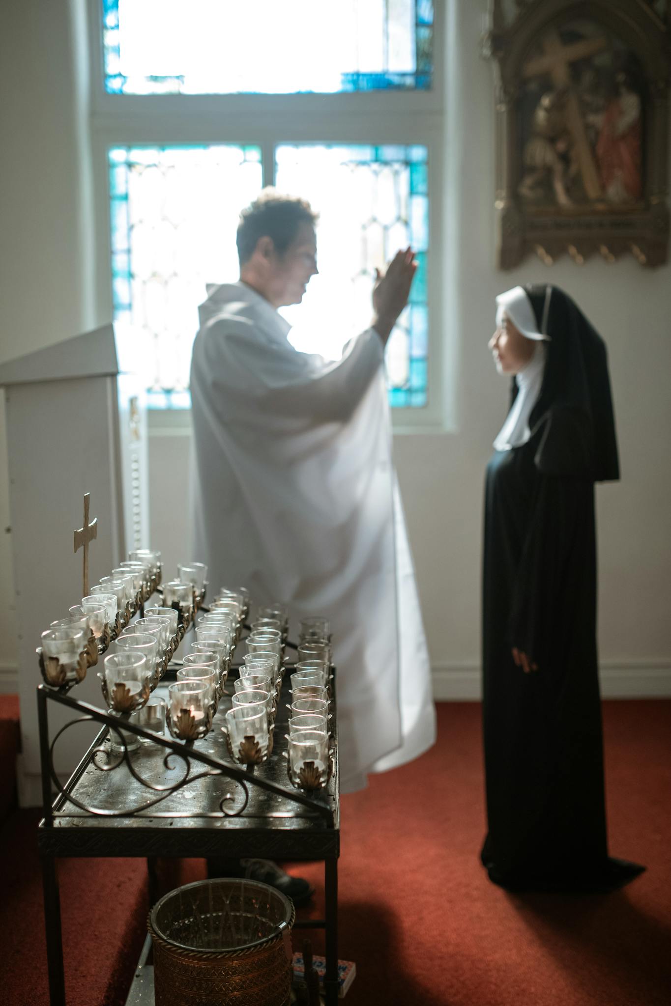 A priest and nun engage in prayer inside a serene church setting.