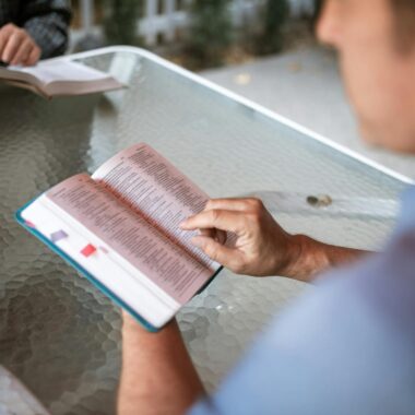 Two adults engaged in Bible study at a glass table outdoors, promoting faith and connection.